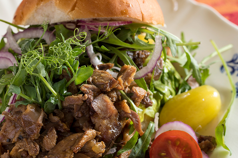 broodje gevuld met gekonfijte gans met rode ui en tomaatje op bord
